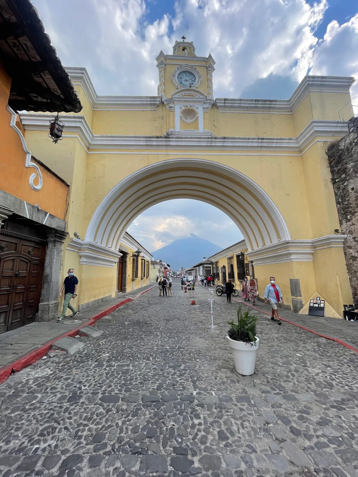 The yellow Santa Catalina Arch over a cobbled street in Antigua, with a volcano visible through it