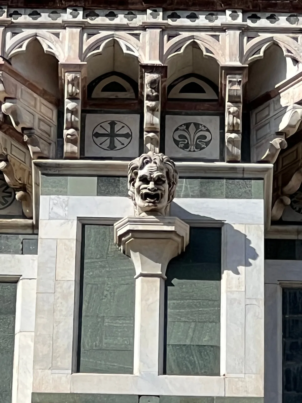 A carved lion's head above an arch on the green, white, and rose marble facade of Florence cathedral
