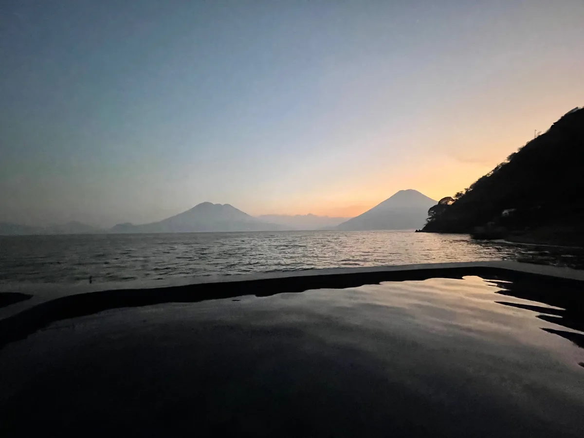 Lake Atitlán at dusk, the water reflecting a volcano and an orange and grey sky
