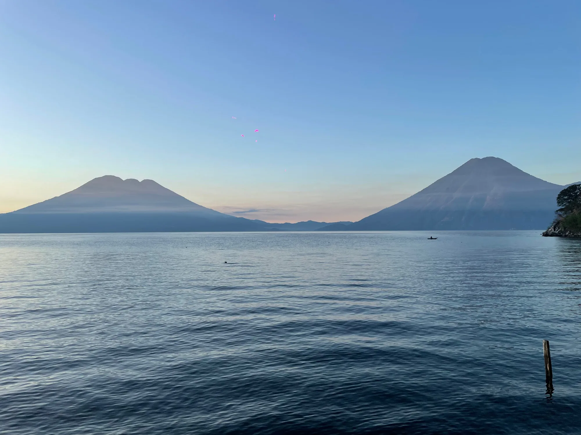 Lake Atitlán, flat and blue, with two volcanoes on the far shore under a clear sky