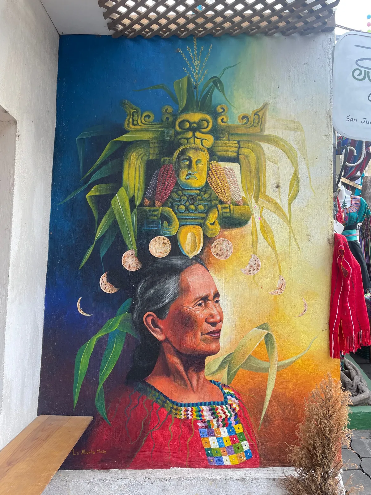 A colourful mural of a woman in traditional dress with a headdress of corn, painted on a wall beside a doorway