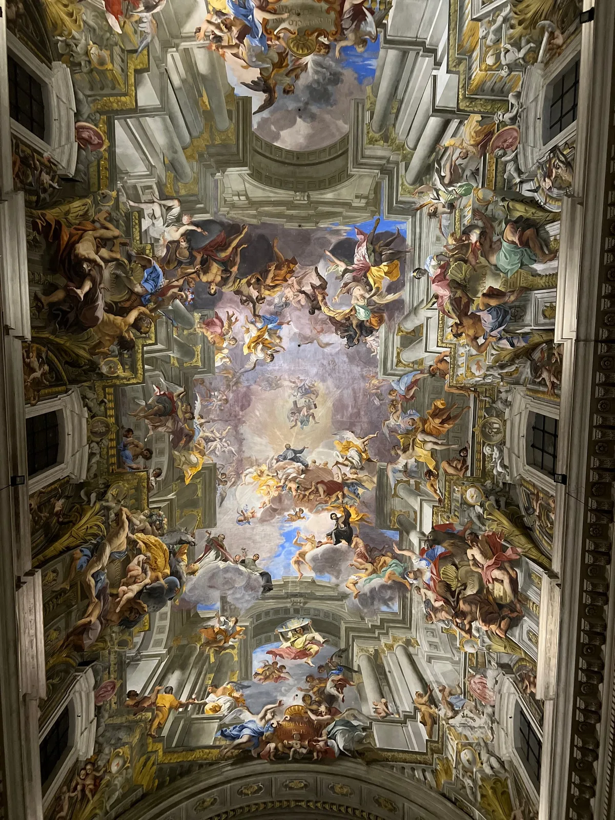 A church ceiling painted with figures and clouds, framed by gilded architecture, photographed straight up