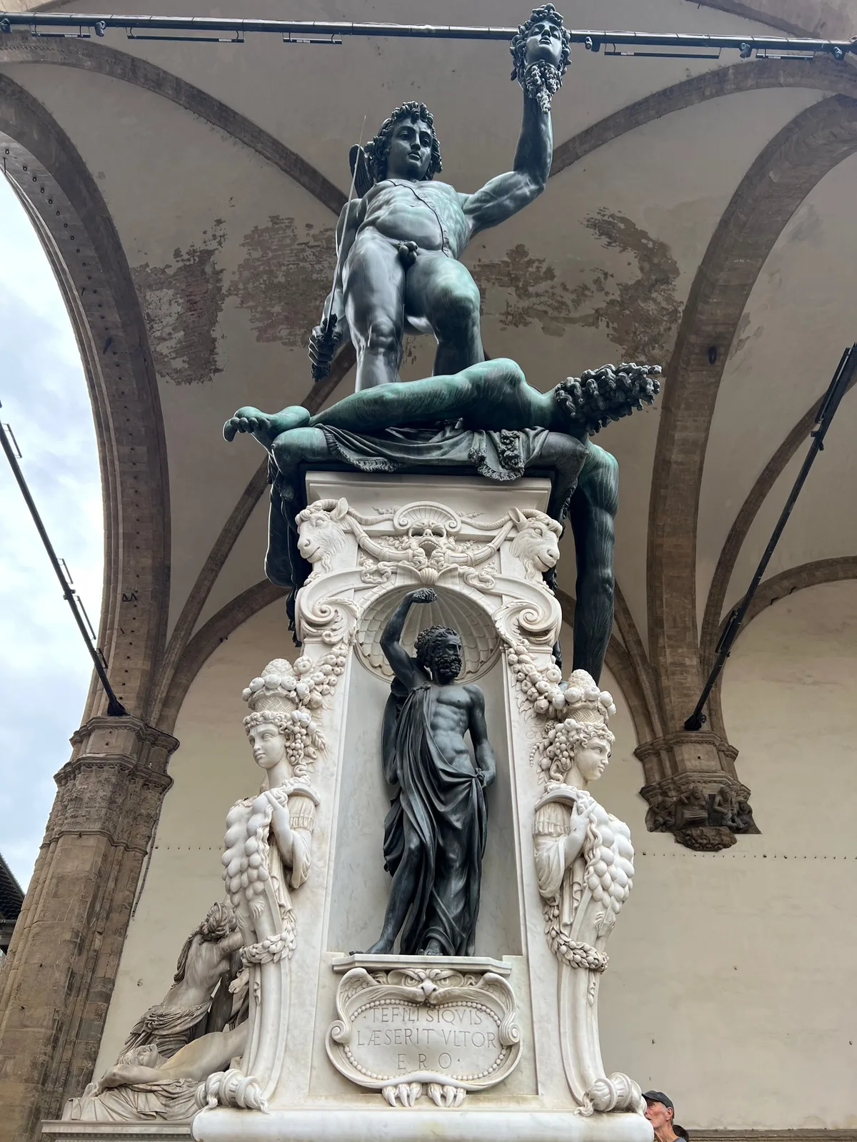 Cellini's bronze Perseus holding up the head of Medusa under the arches of the Loggia dei Lanzi, with a crowd in the piazza behind