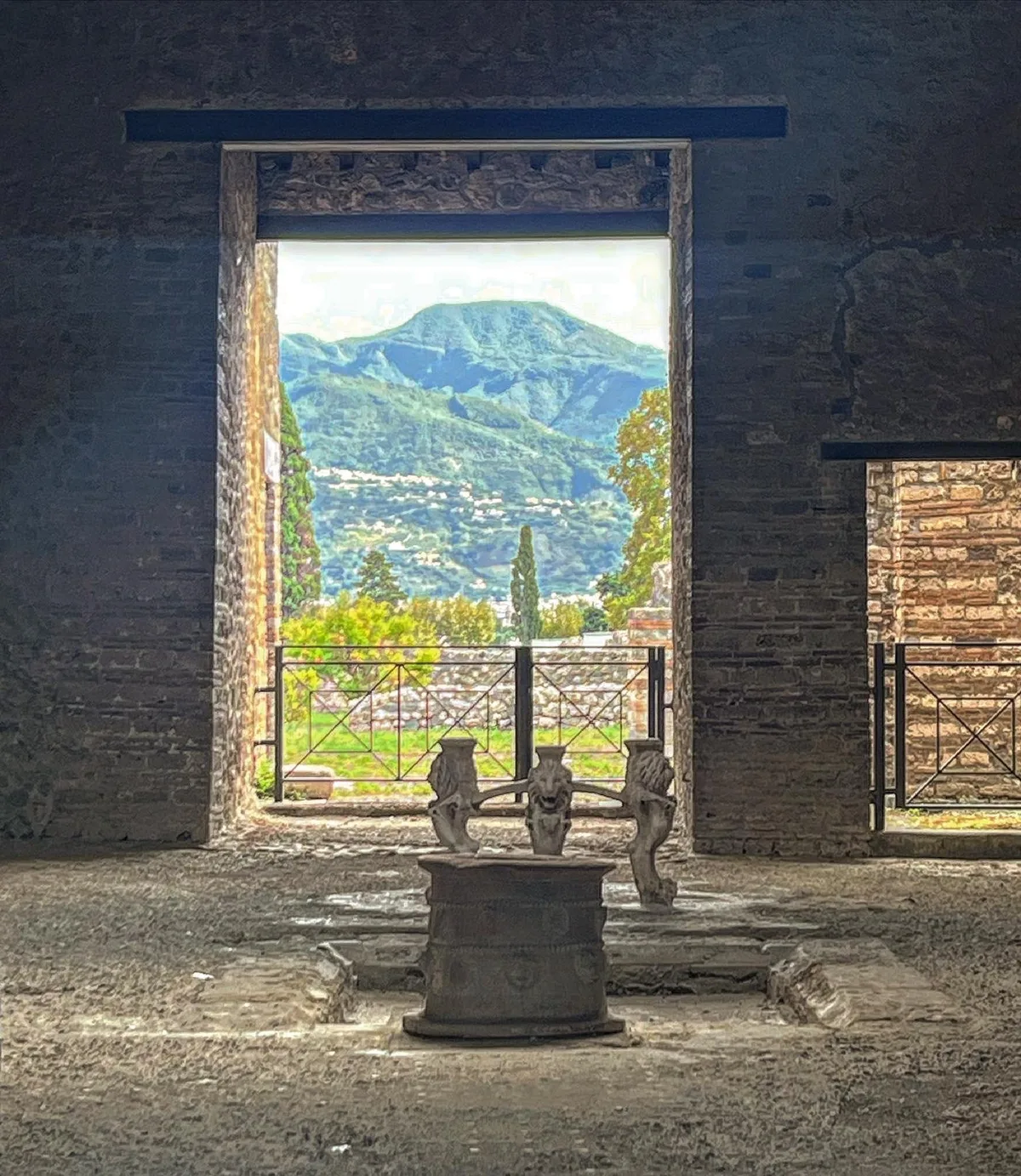 A stone doorway in Pompeii framing a view of green hills and sky, with a stone pedestal in the opening