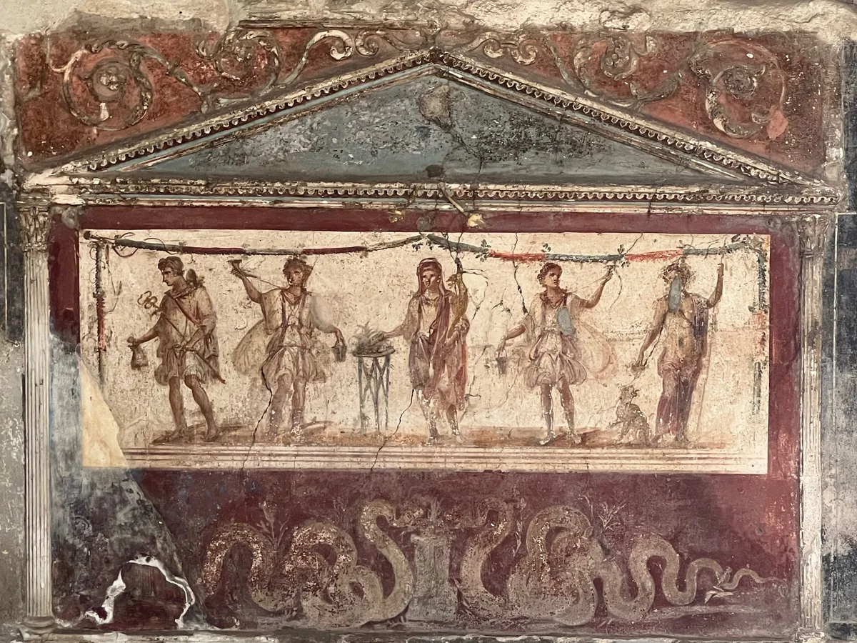 A painted frieze on a Pompeii wall: figures on a red ground with a blue band above, weathered but clear