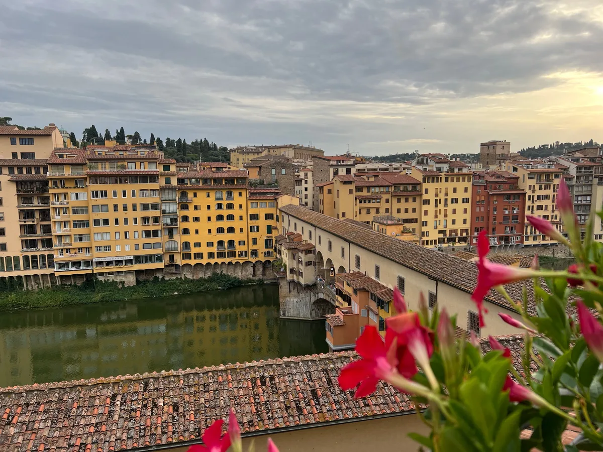 The Ponte Vecchio and its stacked shops across the Arno, with red geraniums in the foreground
