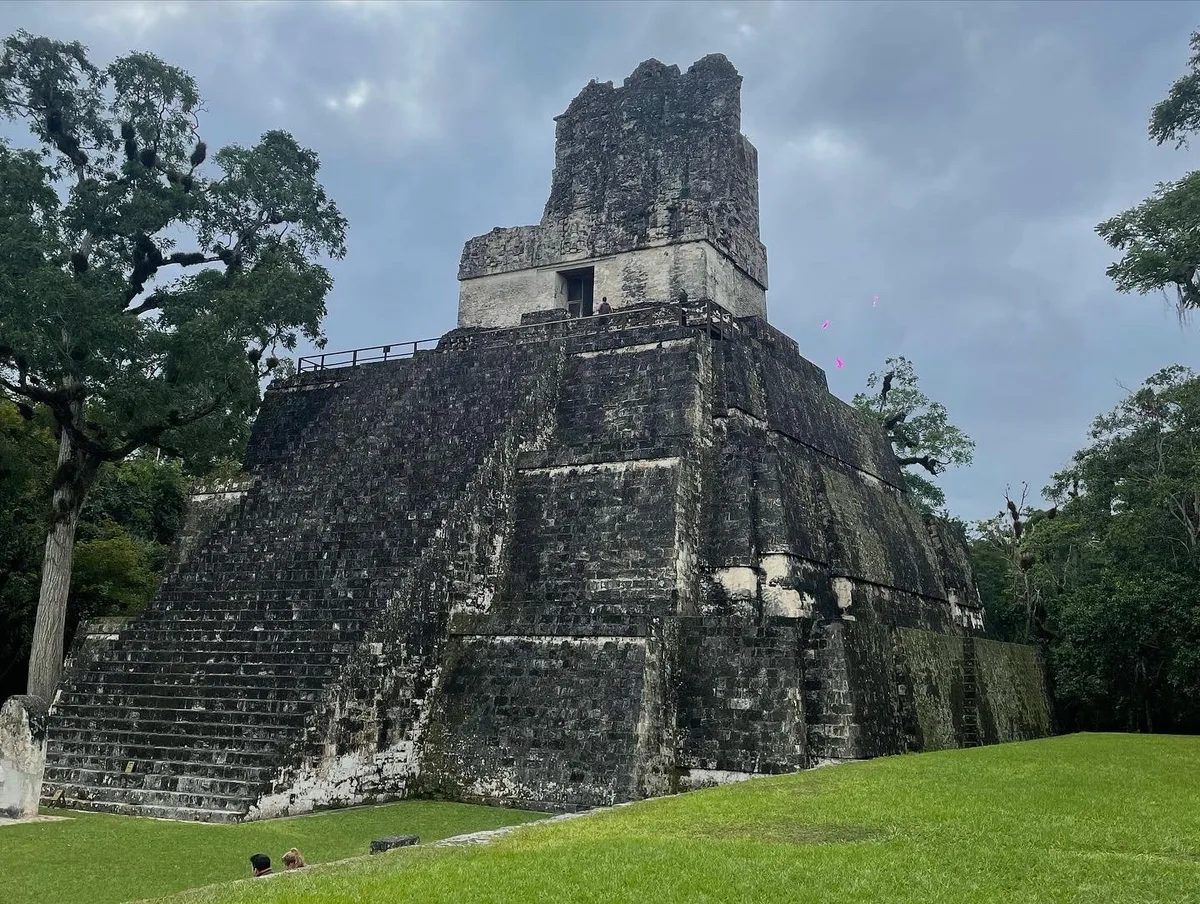 A stone temple at Tikal with a tall roof comb, seen from the grass plaza in front of it